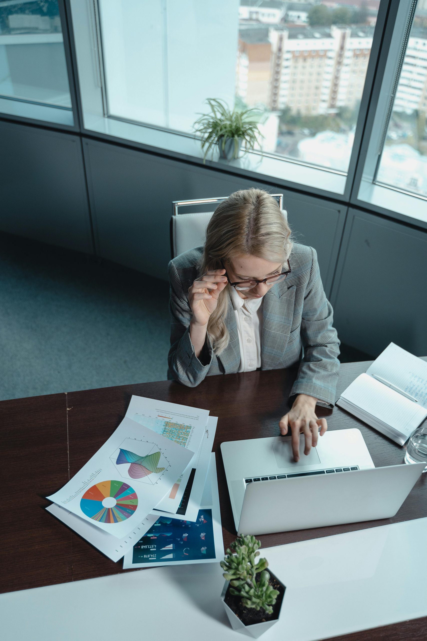 Top view of a businesswoman analyzing data on her laptop in a modern office with charts on the desk.