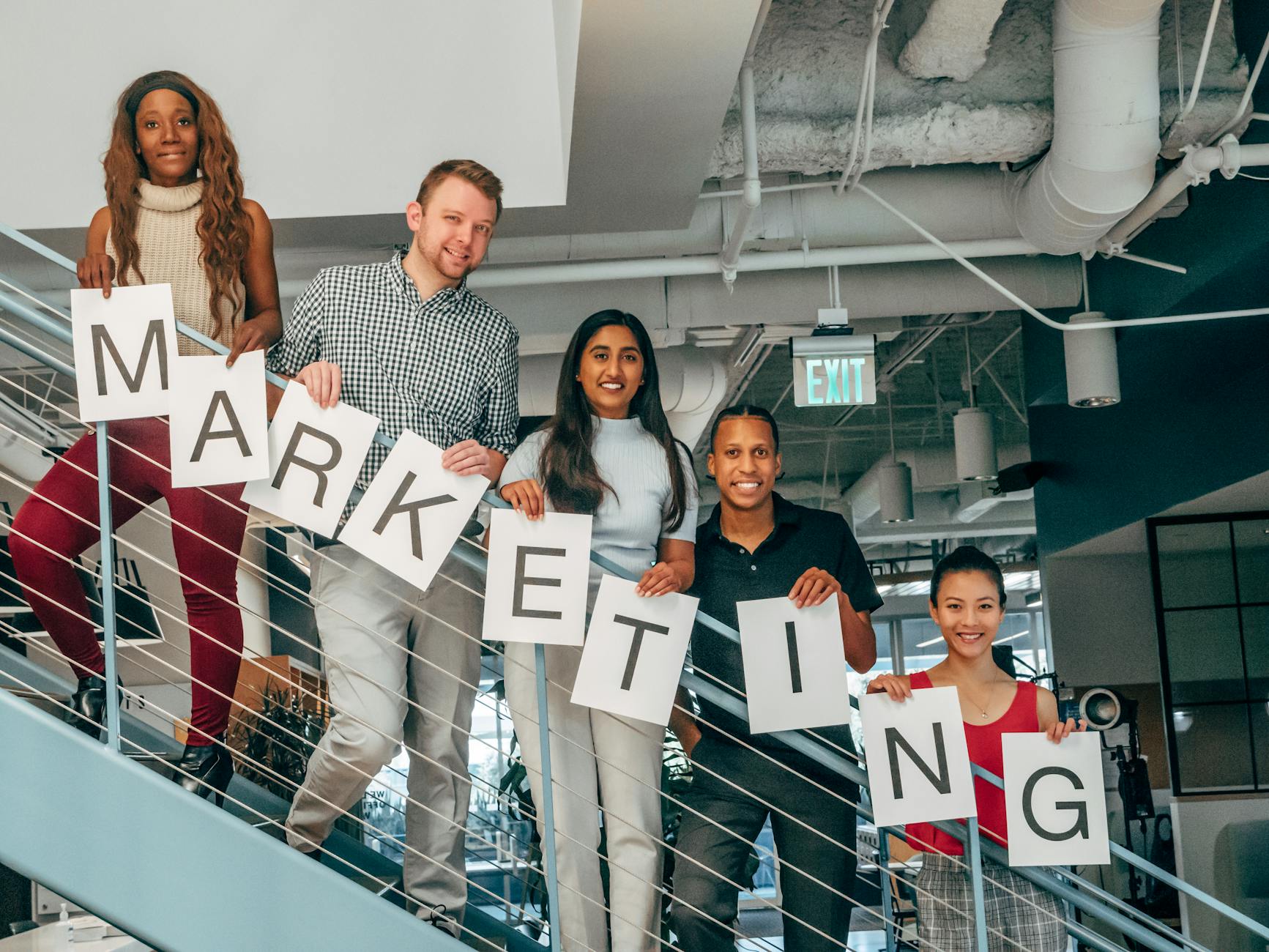 A diverse group of professionals holding a marketing sign in a modern office setting.